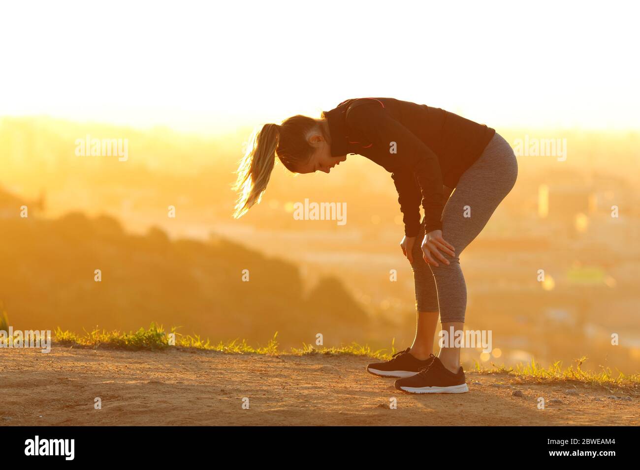 Side view portrait of a tired runner resting after exercise in city outskirts at sunset Stock Photo