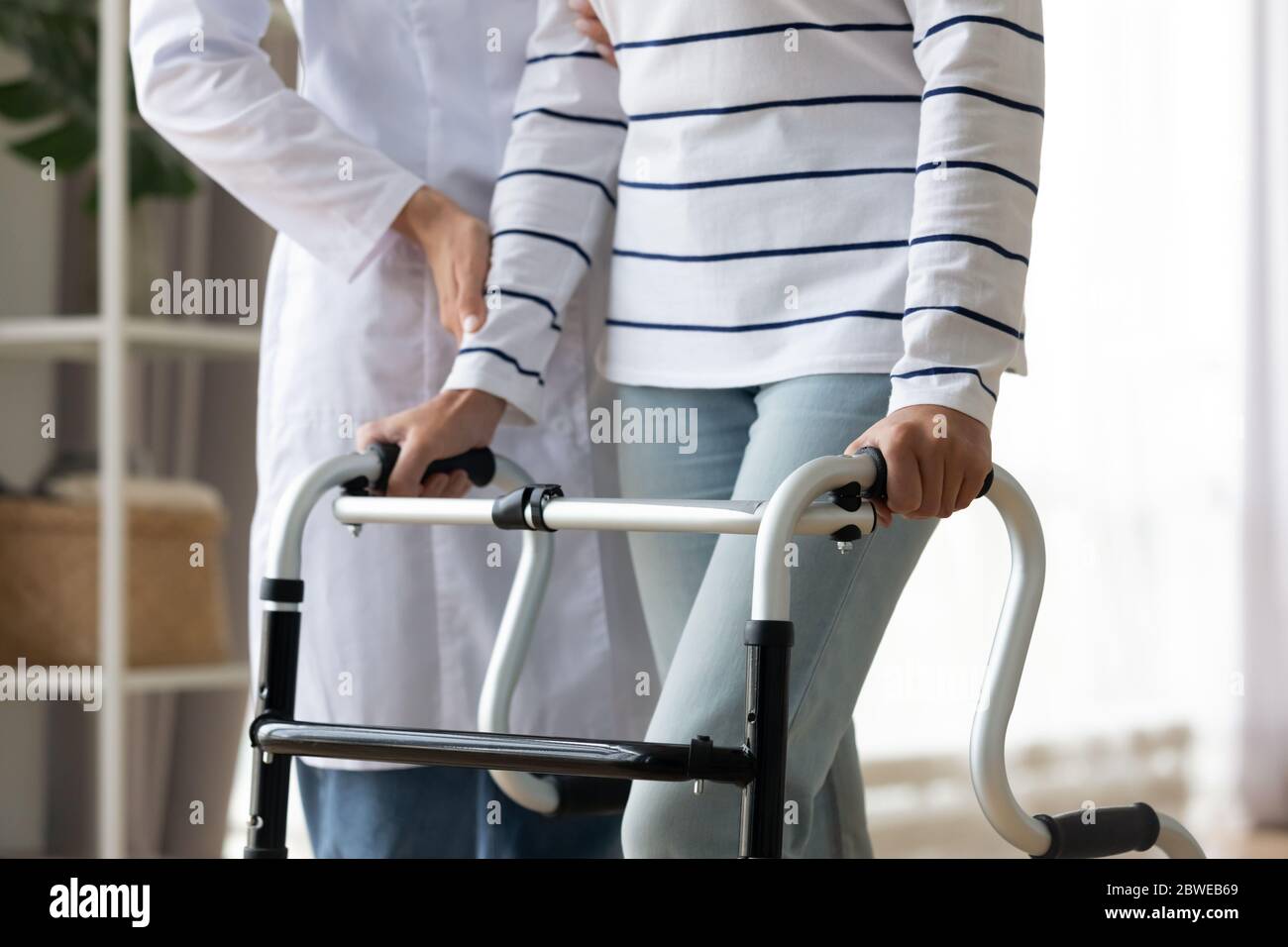 Cropped image caregiver helping to disabled patient walking with rollator Stock Photo