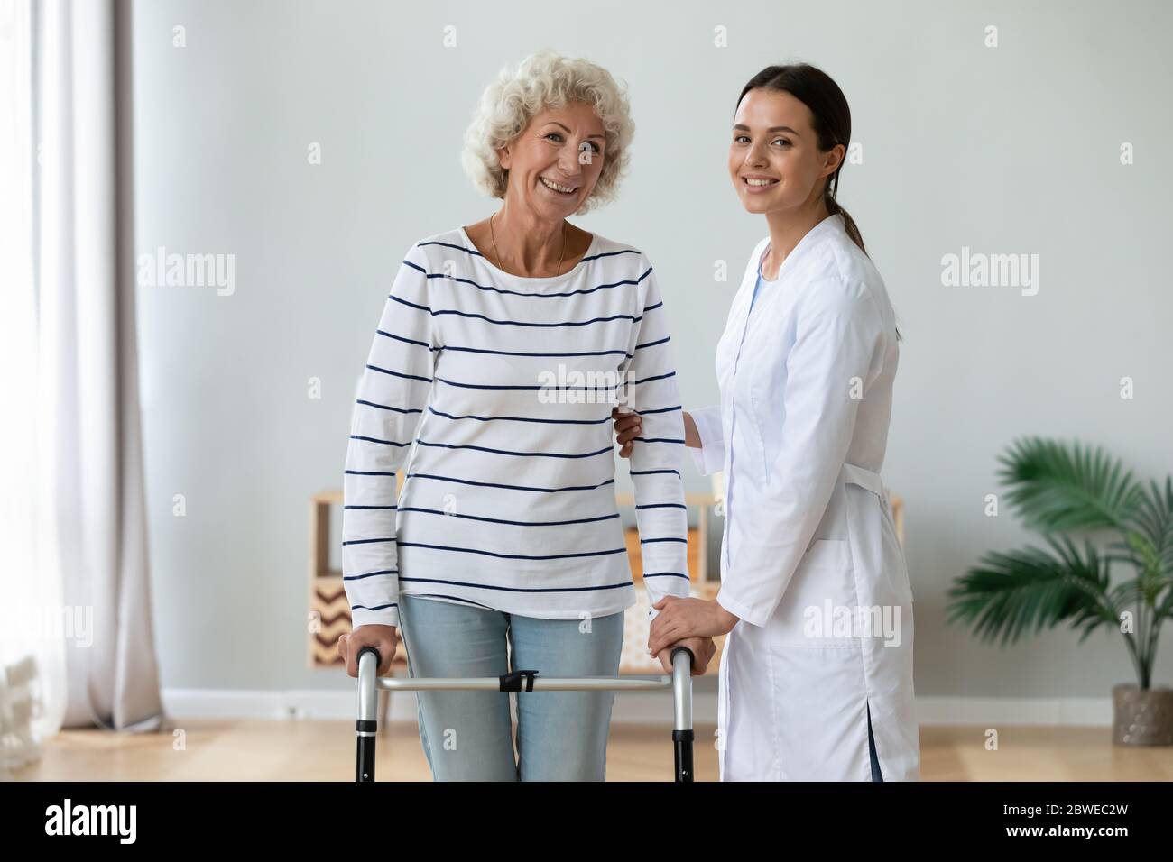 Elderly woman holding rollator feels satisfied after therapy with physiotherapist Stock Photo