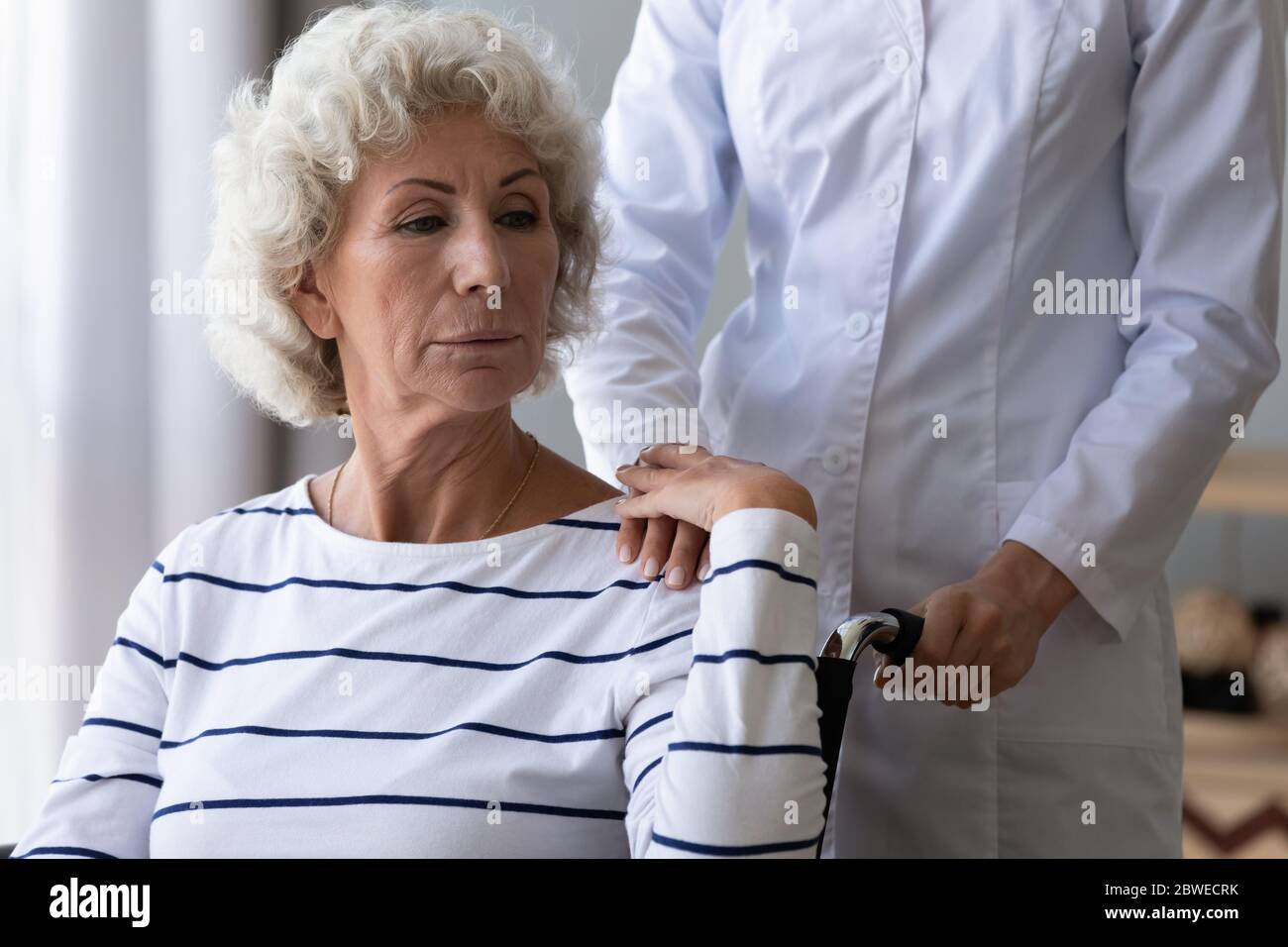 Sad handicapped woman sitting in wheelchair holding hand of caregiver Stock Photo