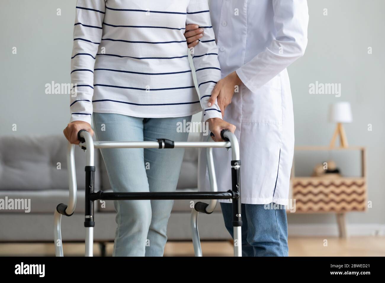 Caregiver helping to disabled aged female patient walk with walker Stock Photo