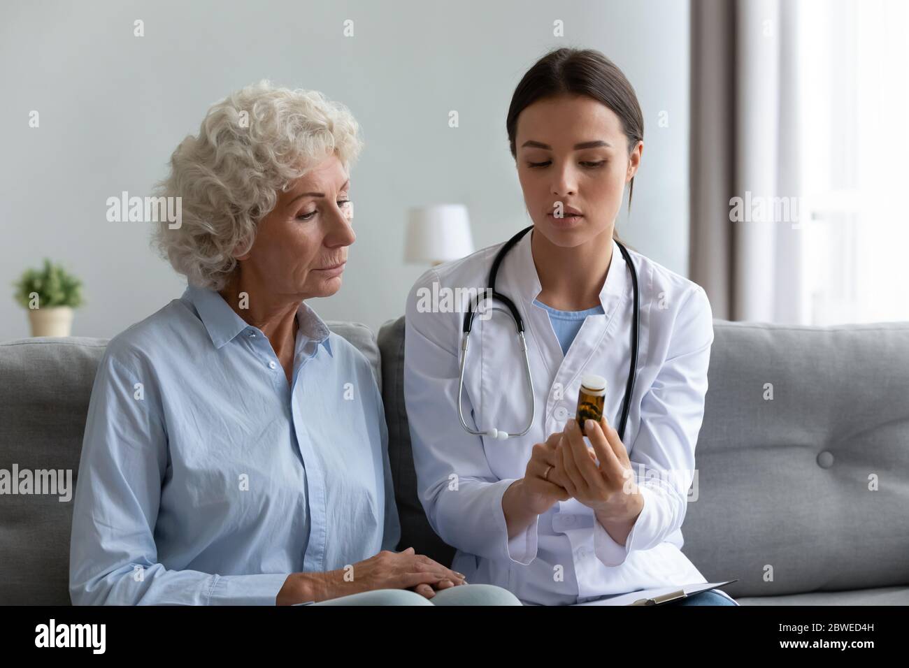 Nurse seated on couch explain to old patient pills dosage Stock Photo