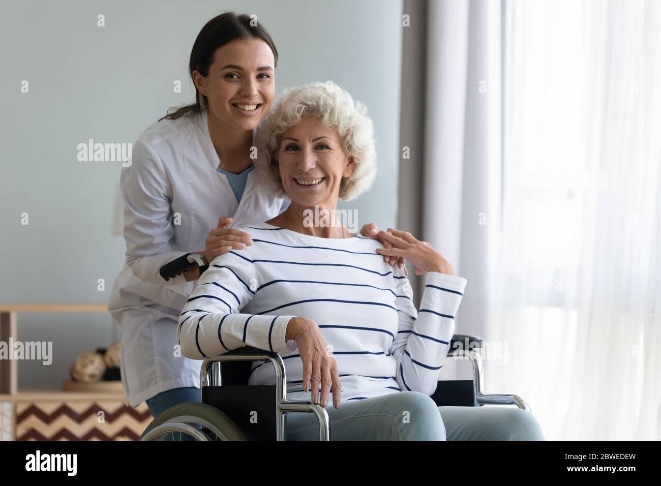 Portrait of satisfied elderly patient in wheelchair and caring caregiver Stock Photo