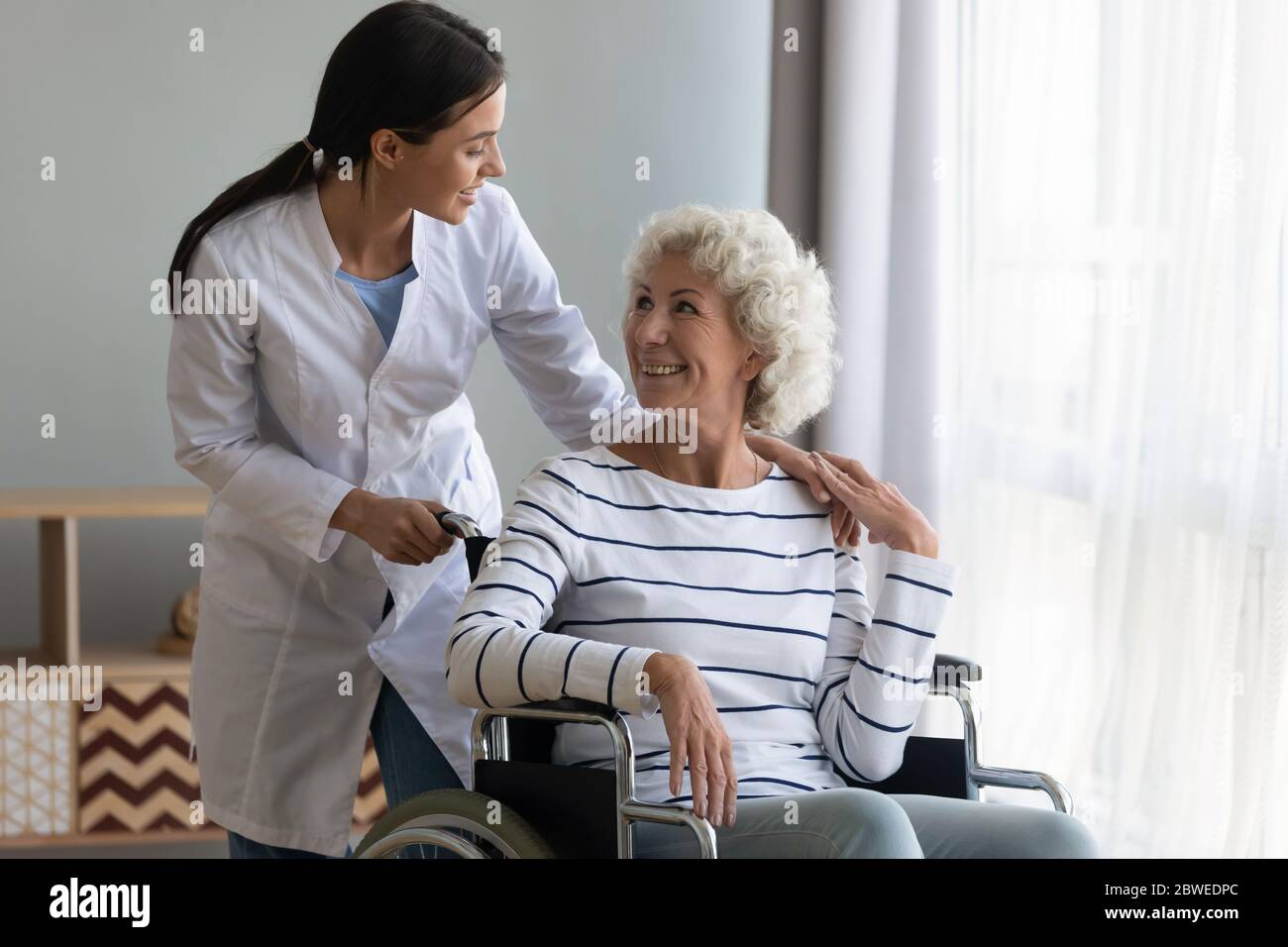 Caregiver smile to disabled patient while she sitting in wheelchair Stock Photo