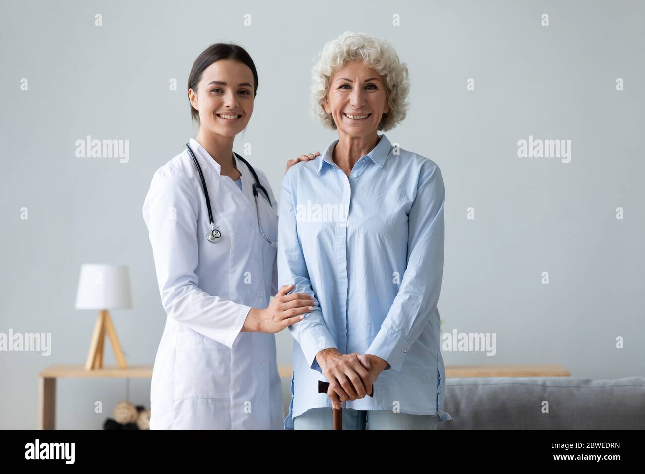 Old patient with walking stick and young caring nurse portrait Stock Photo