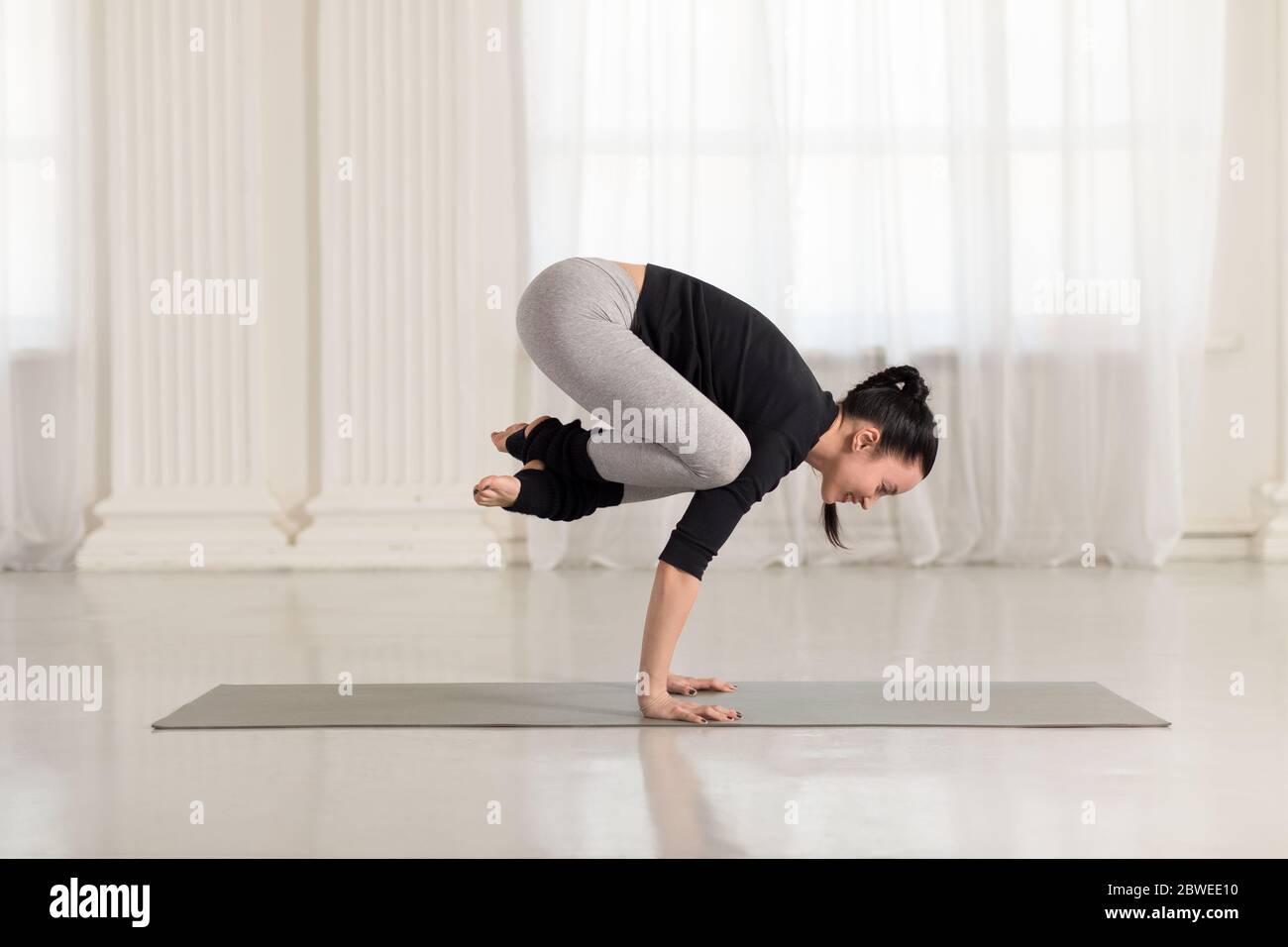 Beautiful young asian woman working out, doing yoga exercise, handstand asana, exercise for arms and wrists strength, Crane Crow Pose, Bakasana Stock Photo