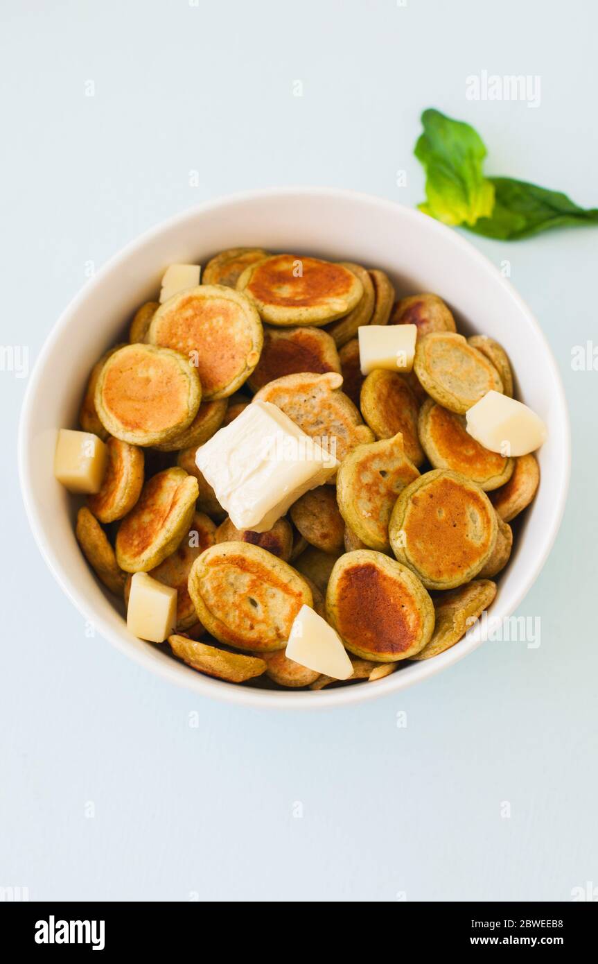 Spinach pancake cereals in a white bowl on a light blue background. Overhead view, close up. Stock Photo