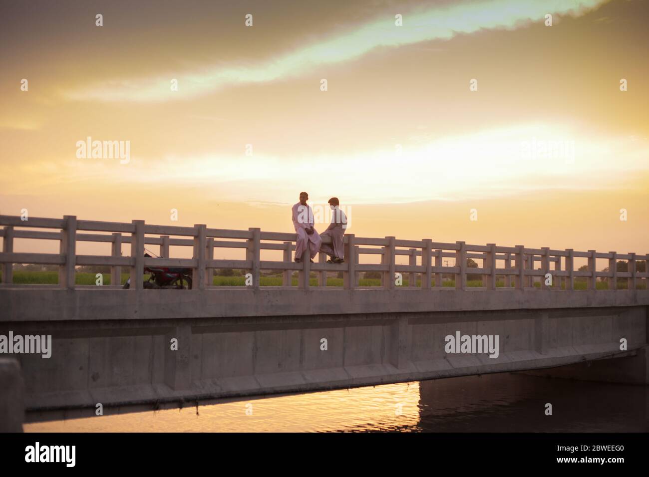 Two Villagers Are Sitting On A Bridge During Sunset, In Moro, Sindh, Pakistan 26/08/2017 Stock Photo