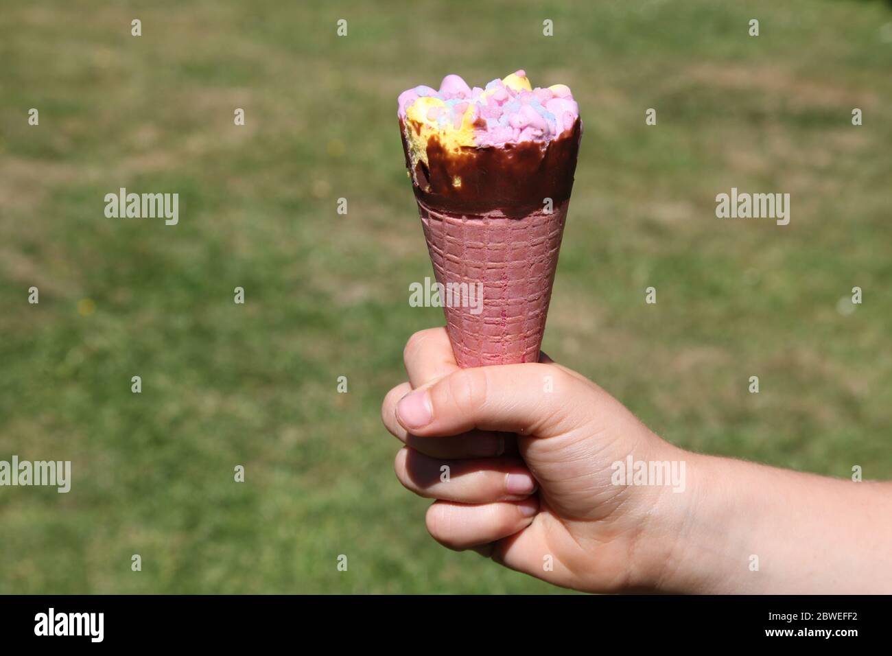Boys hand holding Tesco Rainbow Ice Cream Cone, daytime, summer, 2020