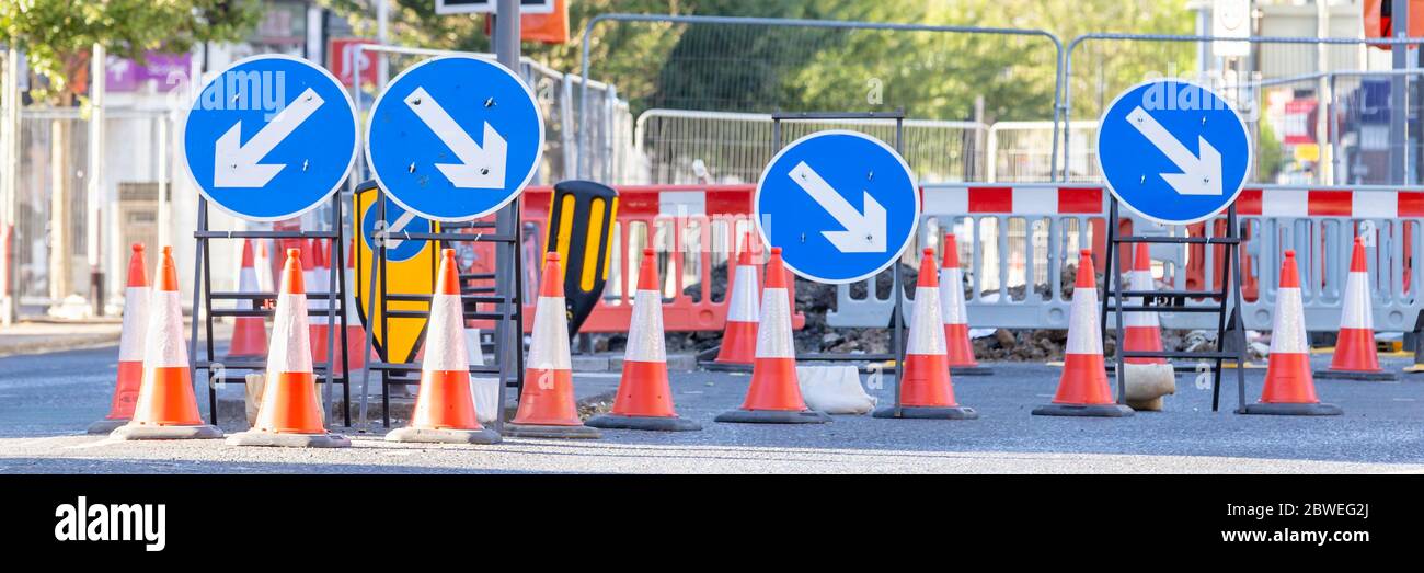 Four Round Blue Road Signs Each Containing a White Arrow Indicating a Mandatory Directional Instruction to Motorists.  Several Traffic cones in Front. Stock Photo