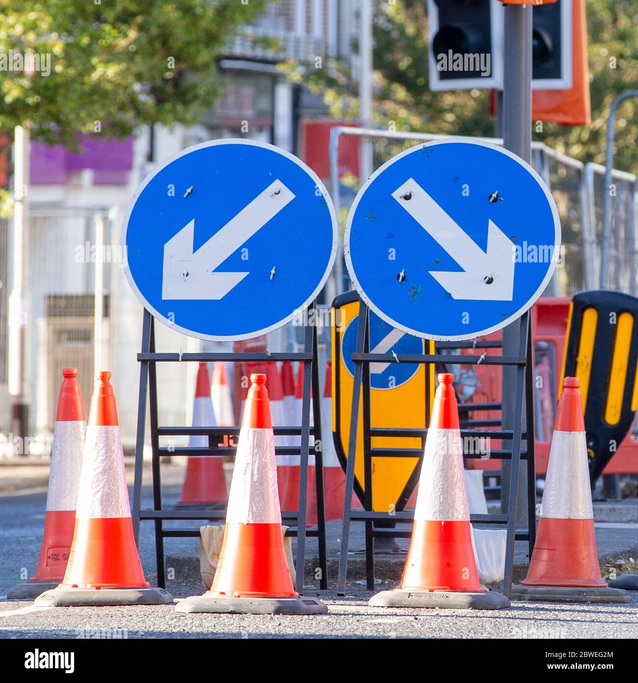 Two Round Blue Road Signs Each Containing a White Arrow Indicating a Mandatory Directional Instruction to Motorists.  Several Traffic cones in Front. Stock Photo