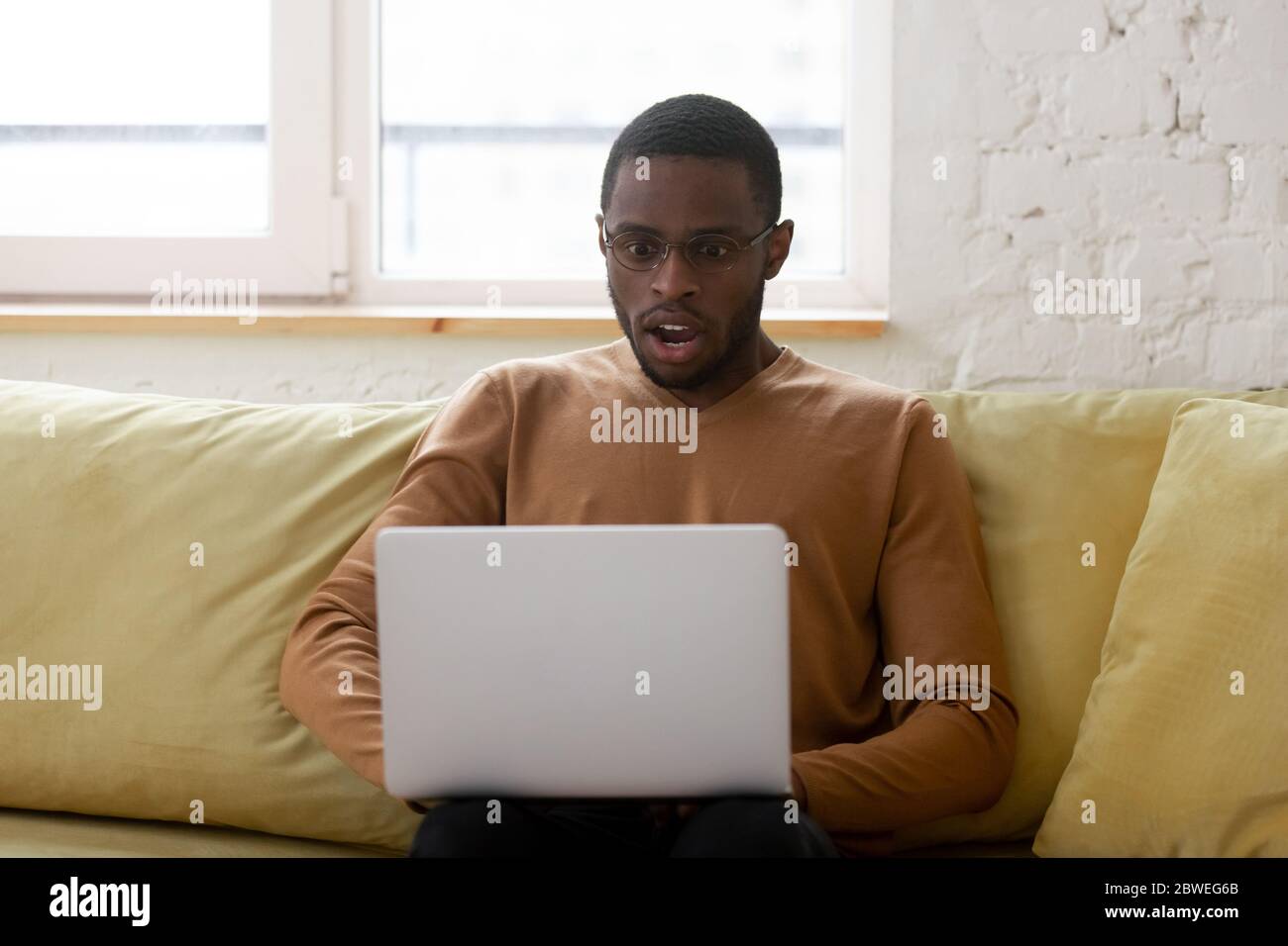 African ethnicity guy gawp at laptop screen feels shocked Stock Photo