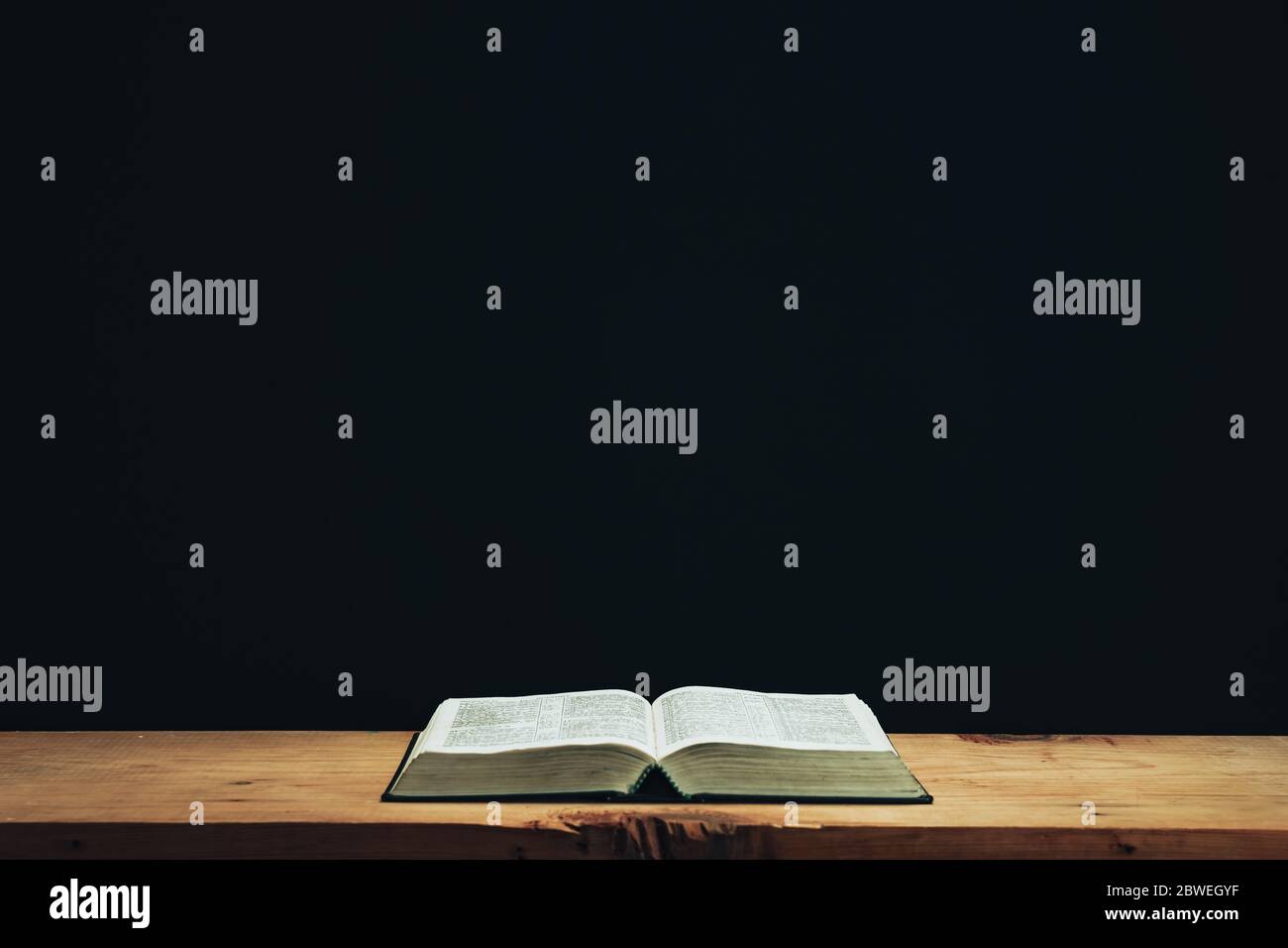 Open Holy Bible on a red old wooden table. Beautiful Black wall background. Stock Photo