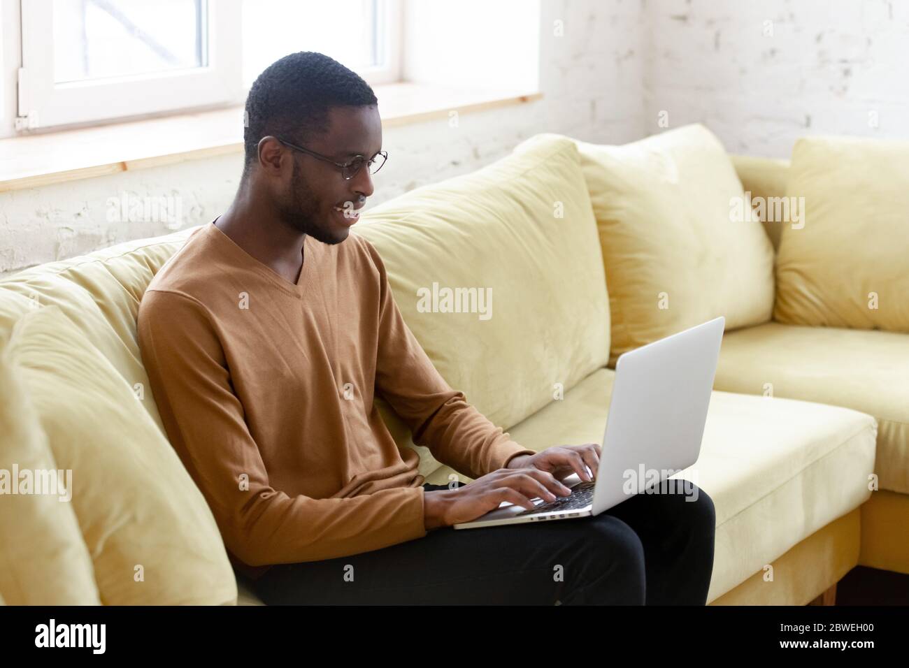 African man sitting on couch typing business letter on laptop Stock Photo