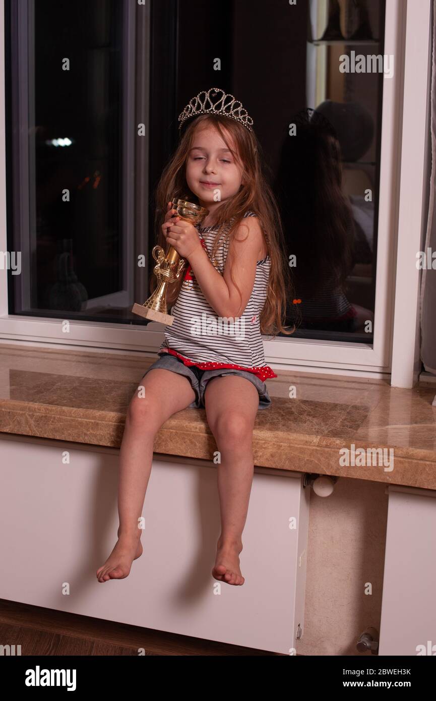 Cute little girl sitting on windowsill. Girl 5 years old with a crown ...