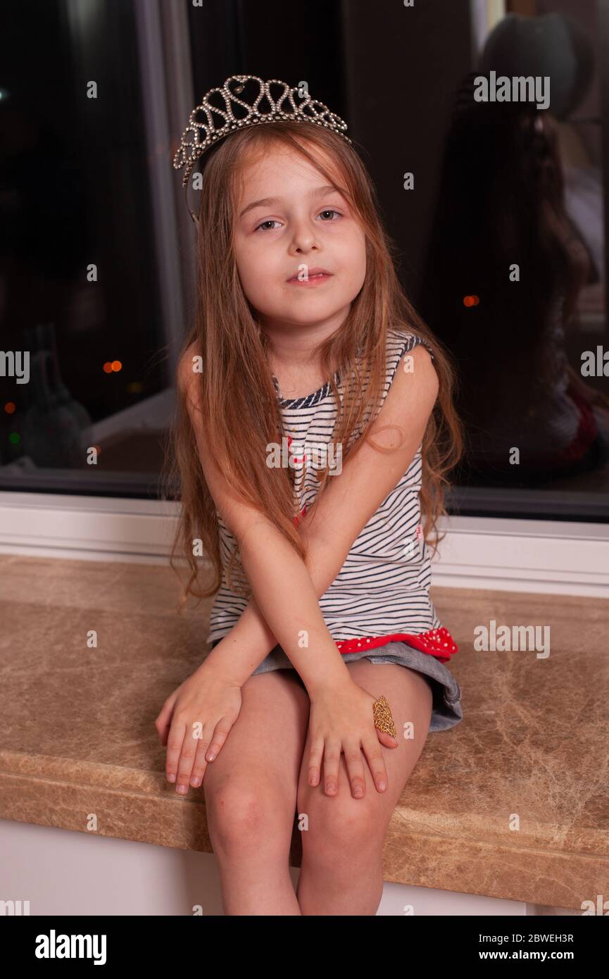 Cute little girl sitting on windowsill. Girl 5 years old with a crown ...