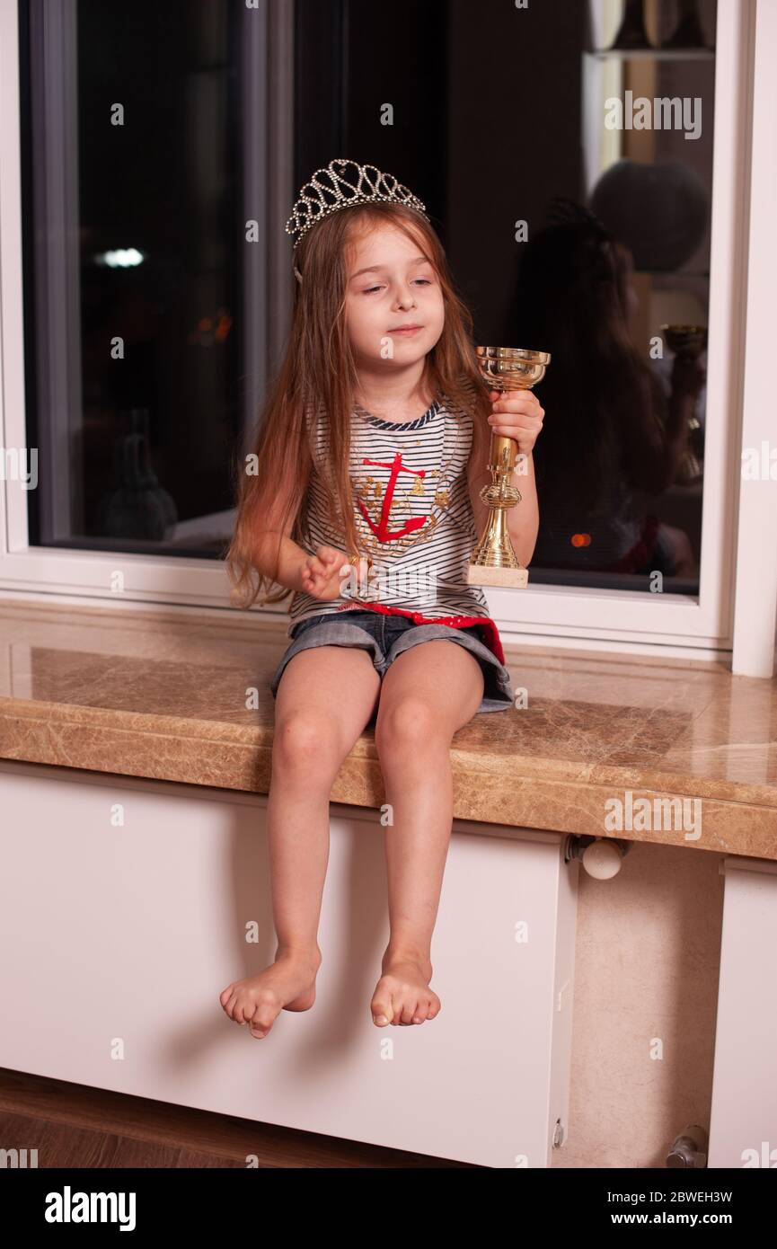 Cute little girl sitting on windowsill. Girl 5 years old with a crown ...