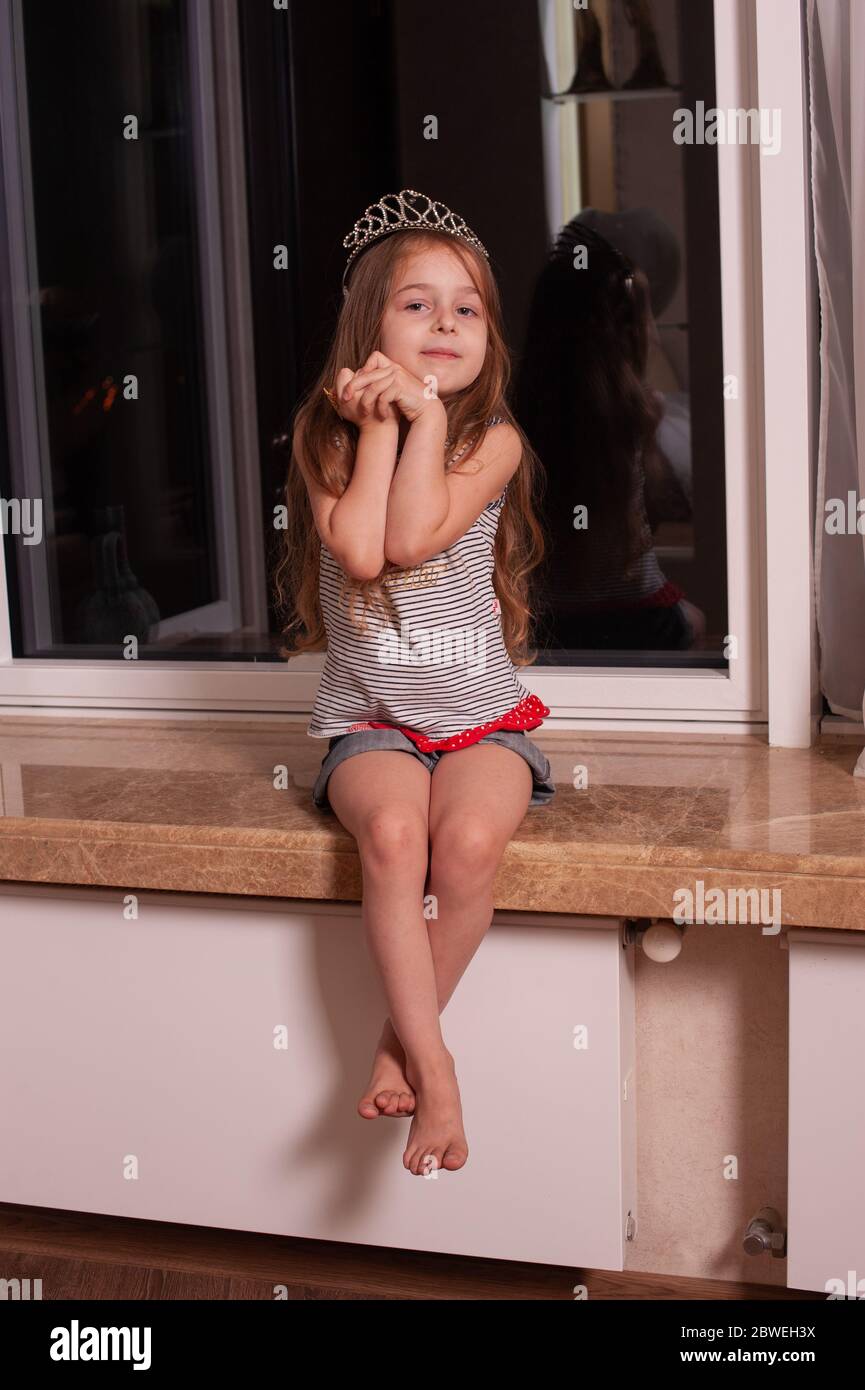 Cute little girl sitting on windowsill. Girl 5 years old with a ...