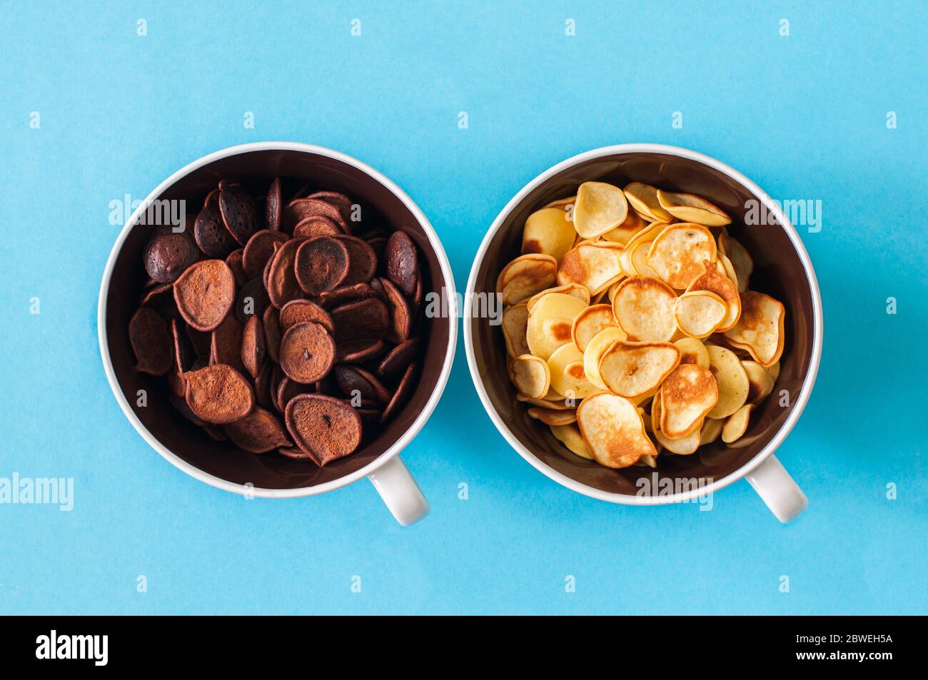 Chocolate and vanilla tiny pancake cereals in a bowls. Top view and flat lay. Blue background. New normal concept. Stock Photo