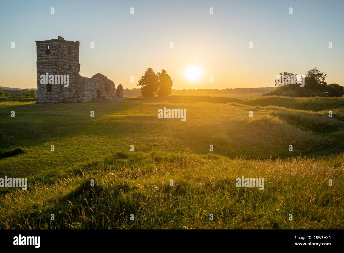 Knowlton Church And Earthworks with sun rising on the horizon illuminating the surrounding