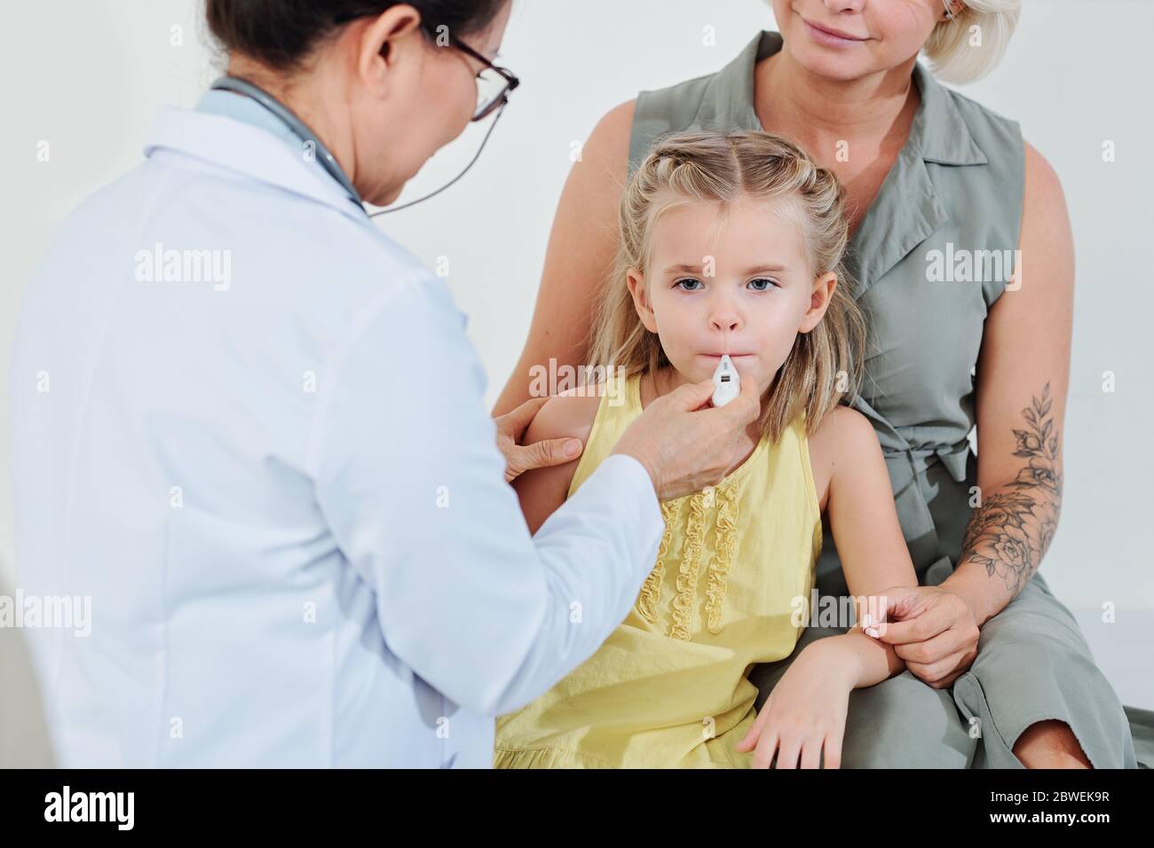Pediatrician putting electronic thermometer in mouth of little girl to