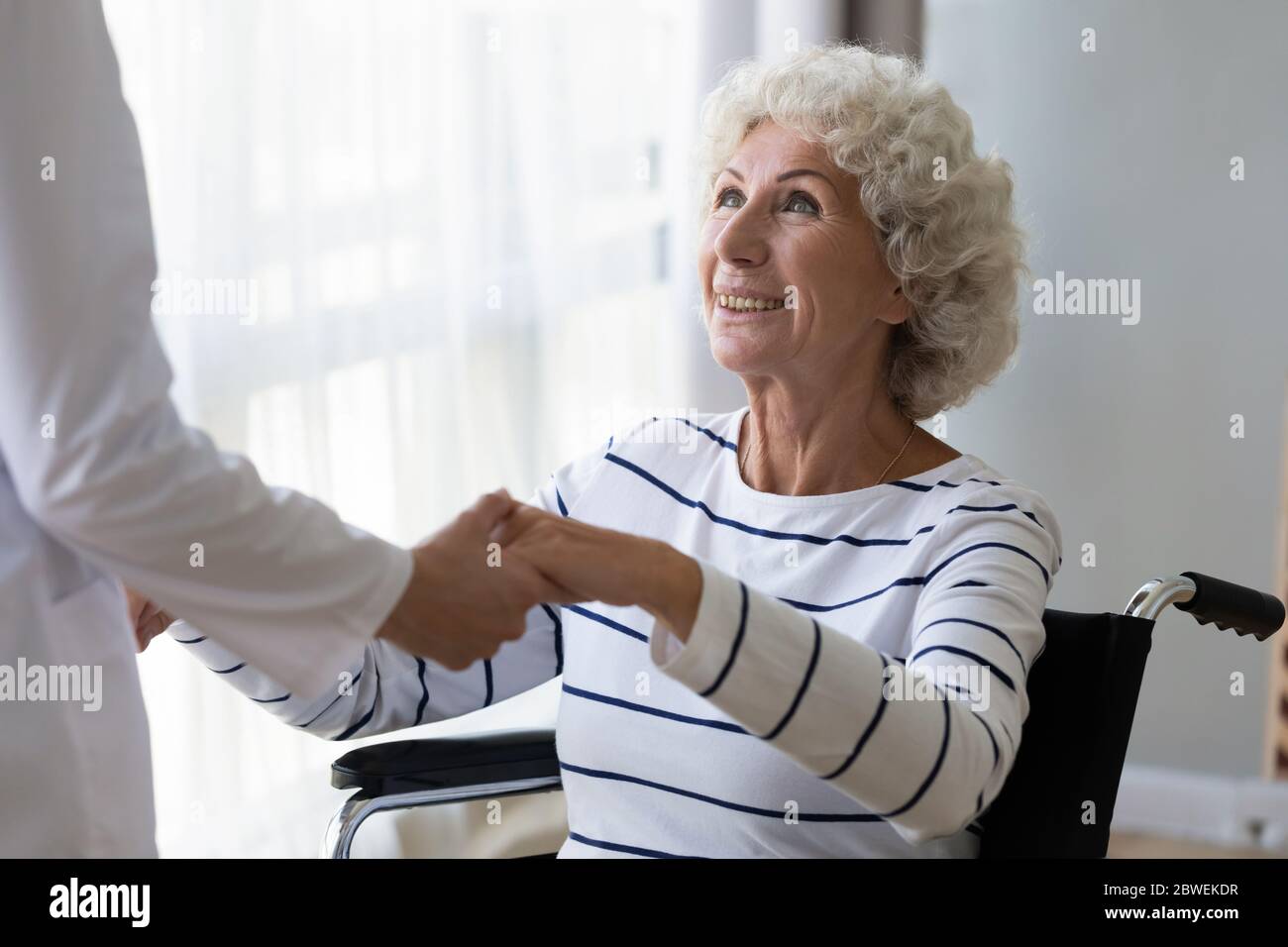 Elderly woman holding hands of caregiver get up from wheelchair Stock Photo
