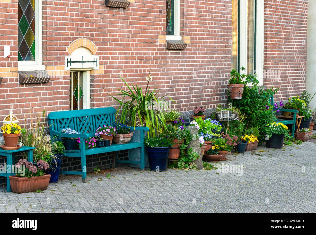 facade of an old Dutch house with various planters and wooden benches on the street with various flower pots filled with flowers placed on it Stock Photo