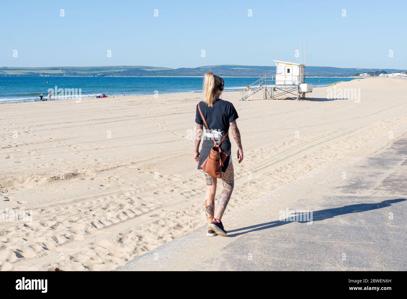 Branksome Chine Beach, Poole, Dorset, UK, 1st June 2020, Weather. More brilliant morning sunshine on the first day of meteorological summer following the sunniest spring on record in the UK. It’s Monday morning and the weekend crowds have gone. A young woman walks along the promenade Credit: Paul Biggins/Alamy Live News Stock Photo