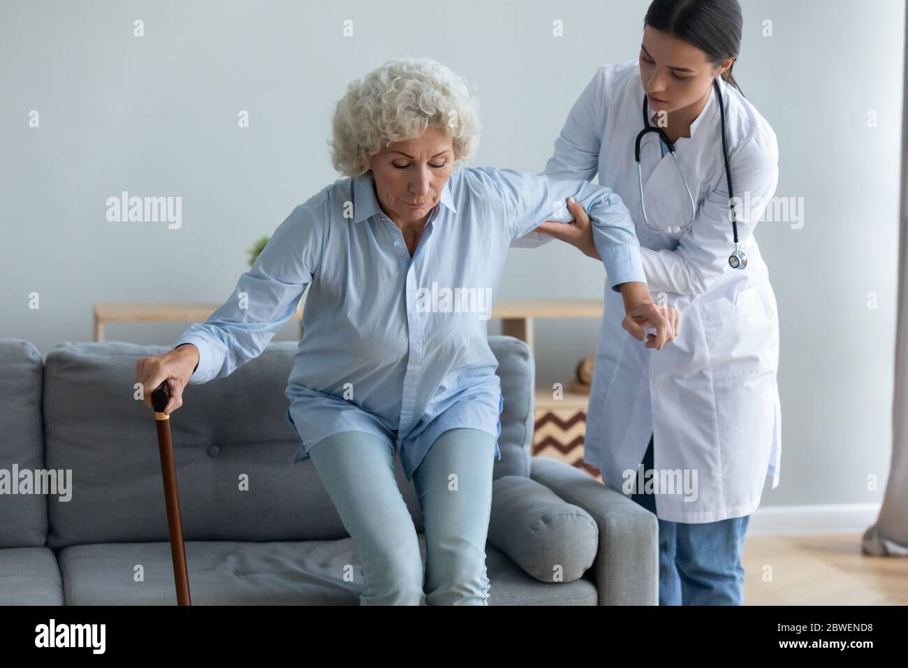 Caring nurse helping to elderly woman get off the couch Stock Photo
