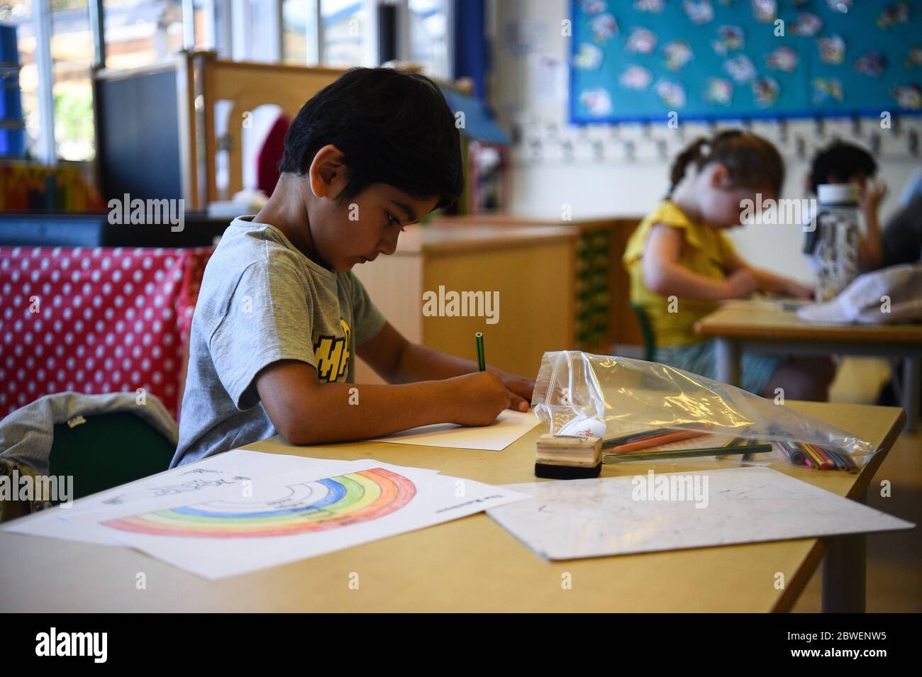 Pupils draw rainbows as they sit at separate desks at Hiltingbury Infant School in Chandler's Ford, Hampshire, as pupils in Reception, Year 1 and Year 6, begin to return to school as part of a wider easing of lockdown measures in England. Stock Photo