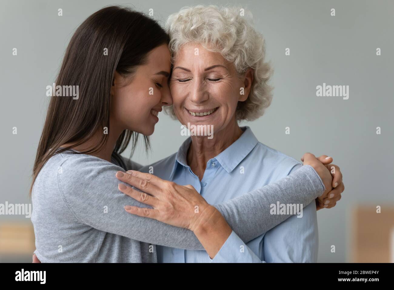 Tender moment of grownup granddaughter elderly grandmother cuddling indoors Stock Photo