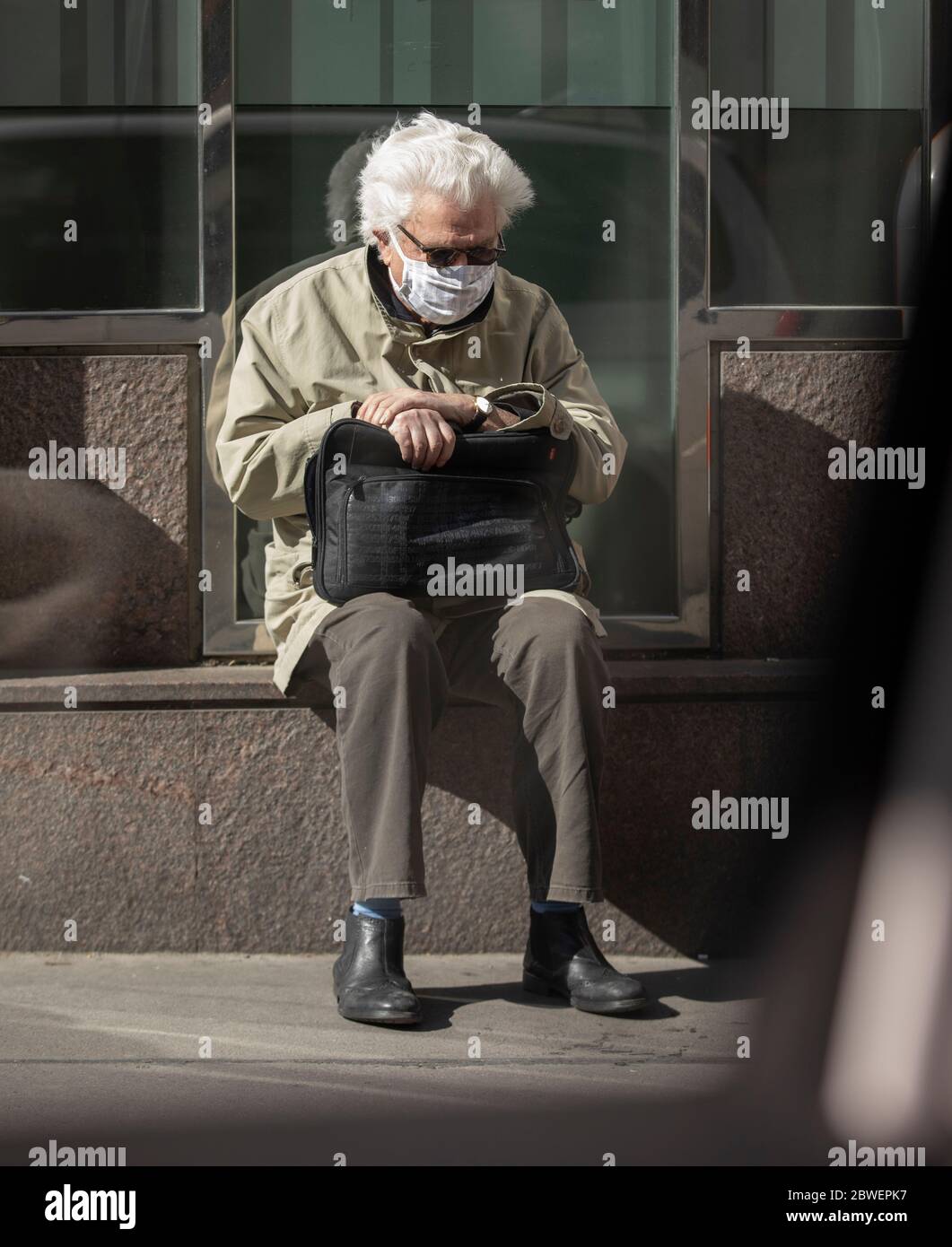 senior man with protective mask sitting outside at  a shopwindow sill  in a sad mood Stock Photo