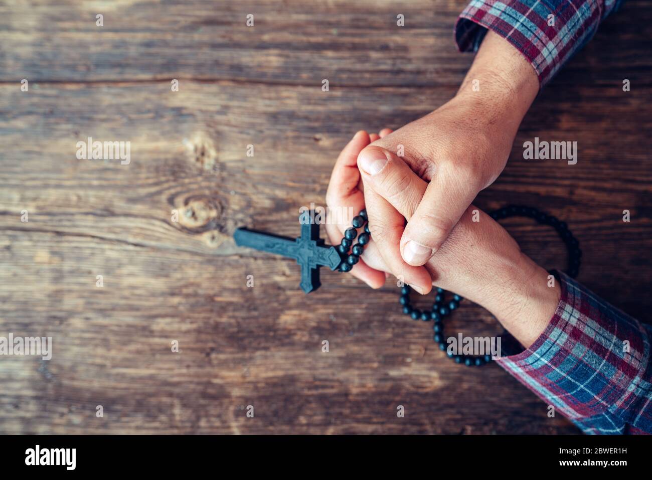 Top view of the Hands are holding a crucifix and praying on a rustic wooden background Stock Photo