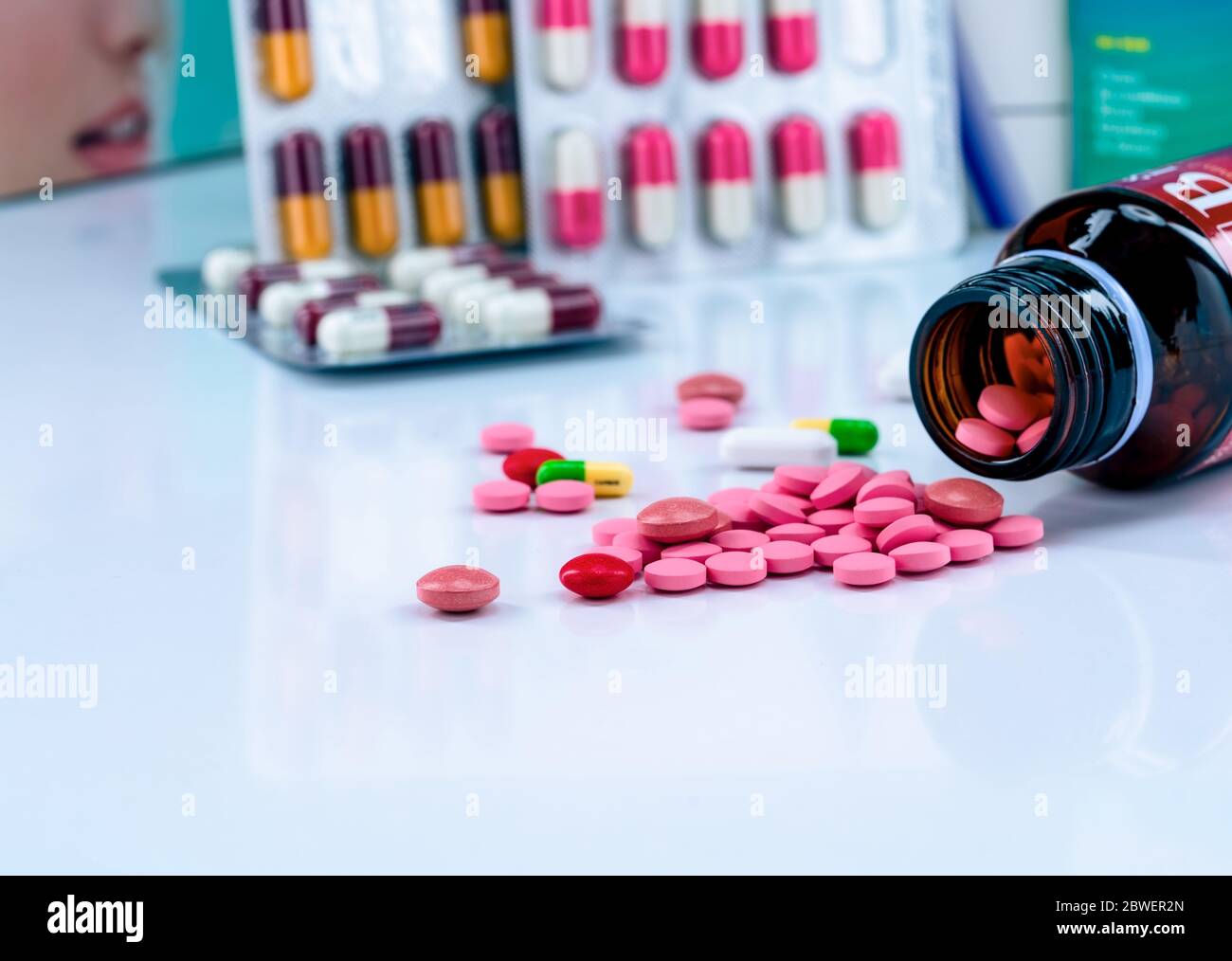 Tablets pills spread out of amber glass drug bottle on blurred capsules in blister pack. Red and pink tablets. Medication use concept. Painkiller Stock Photo