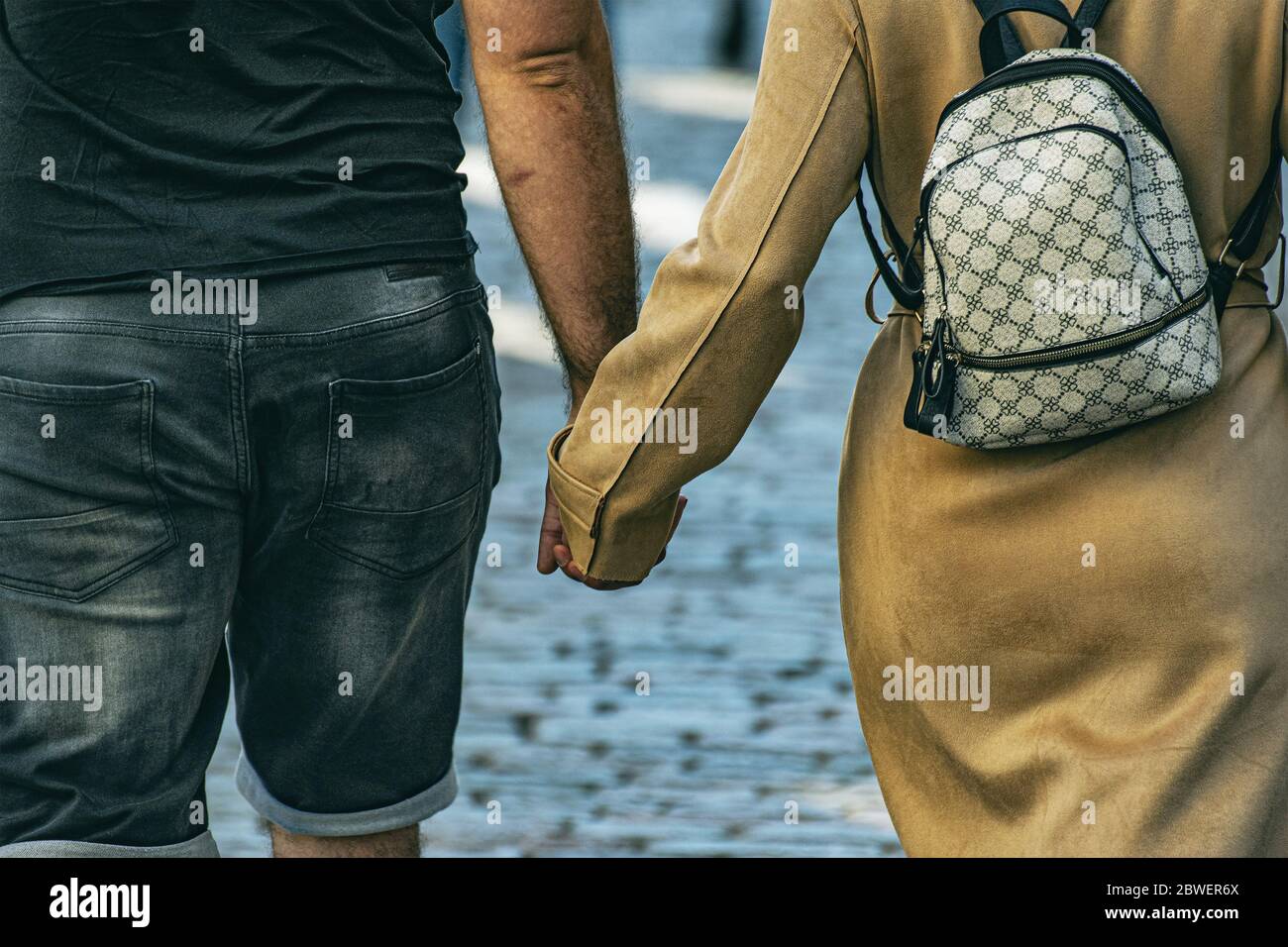 rear view of a couple holding hands and walking on the street ...