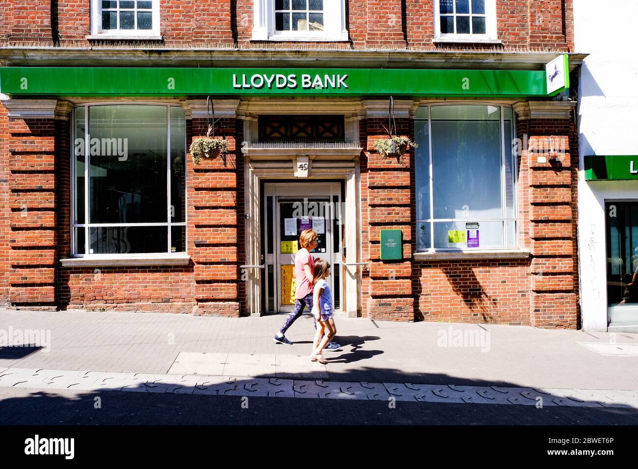 Mother And Young Daughter Walking Past High Street Branch Of Lloyds Bank Stock Photo