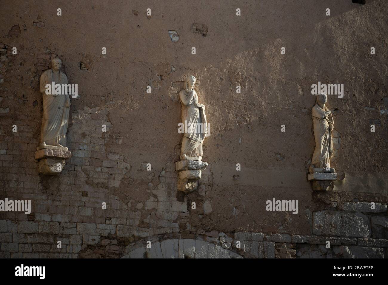 three marble statues of the Roman age placed on the Porta Consolare in the city of Spello in Umbria, Italy. Stock Photo