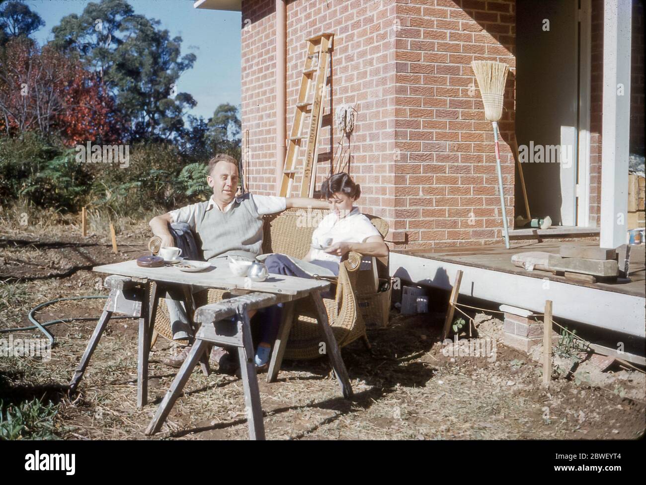 Sydney Australia 1959: A young married couple sit in the back yard of their newly completed red brick home in Turramurra on Sydney's north shore in Australia. Grace Bros (department store) Home Plans Service, established in association with the Sunday Telegraph Newspaper, Sydney, was launched in April 1954 and this home is based on one of those plans. Stock Photo