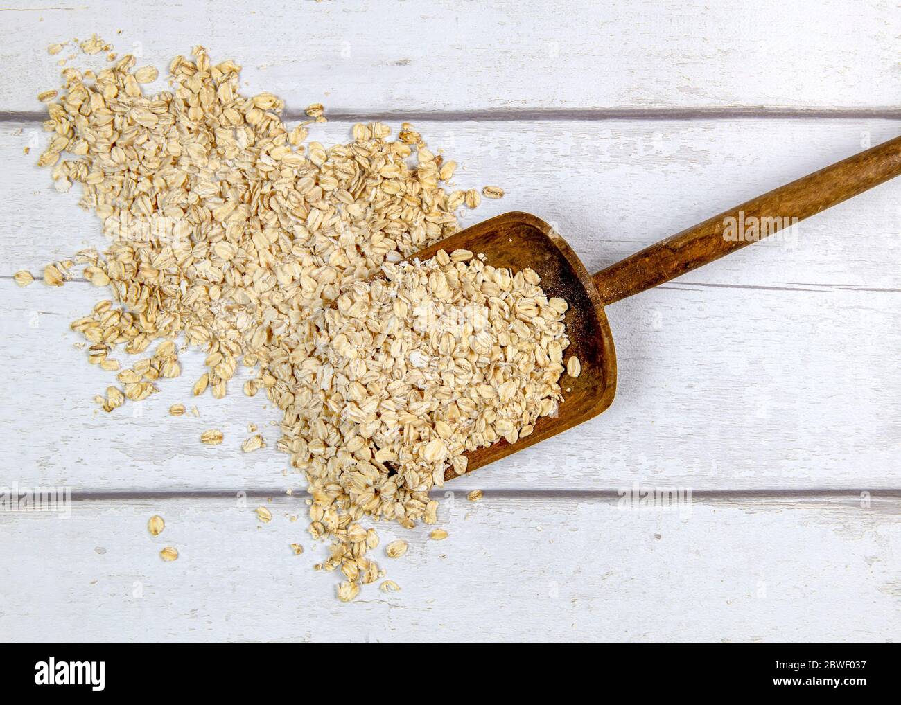 Top view of rustic spade taking portion of raw oatmeal from heap on white lumber table  shoot for text overlay and recipes Stock Photo