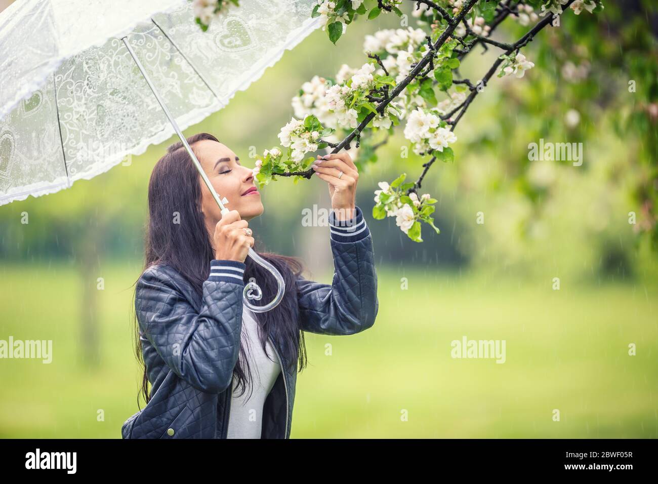 Woman smells tree flowers on during a spring rainy day in the 