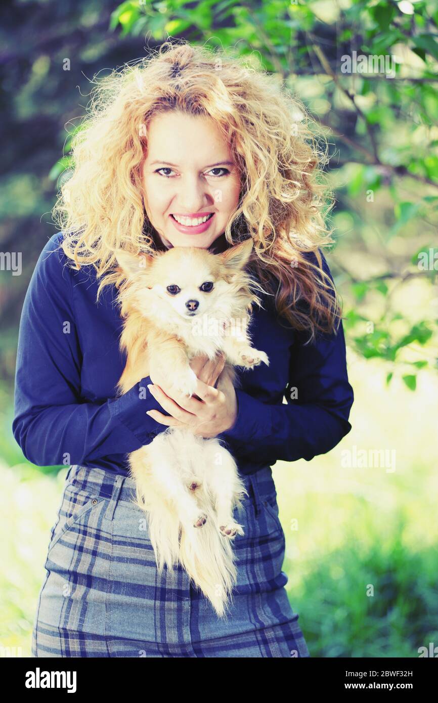 Blond young woman, business dressed, holding a long-haired chihuahua dog outdoor, on a green natural background ( with artistic filter ) Stock Photo
