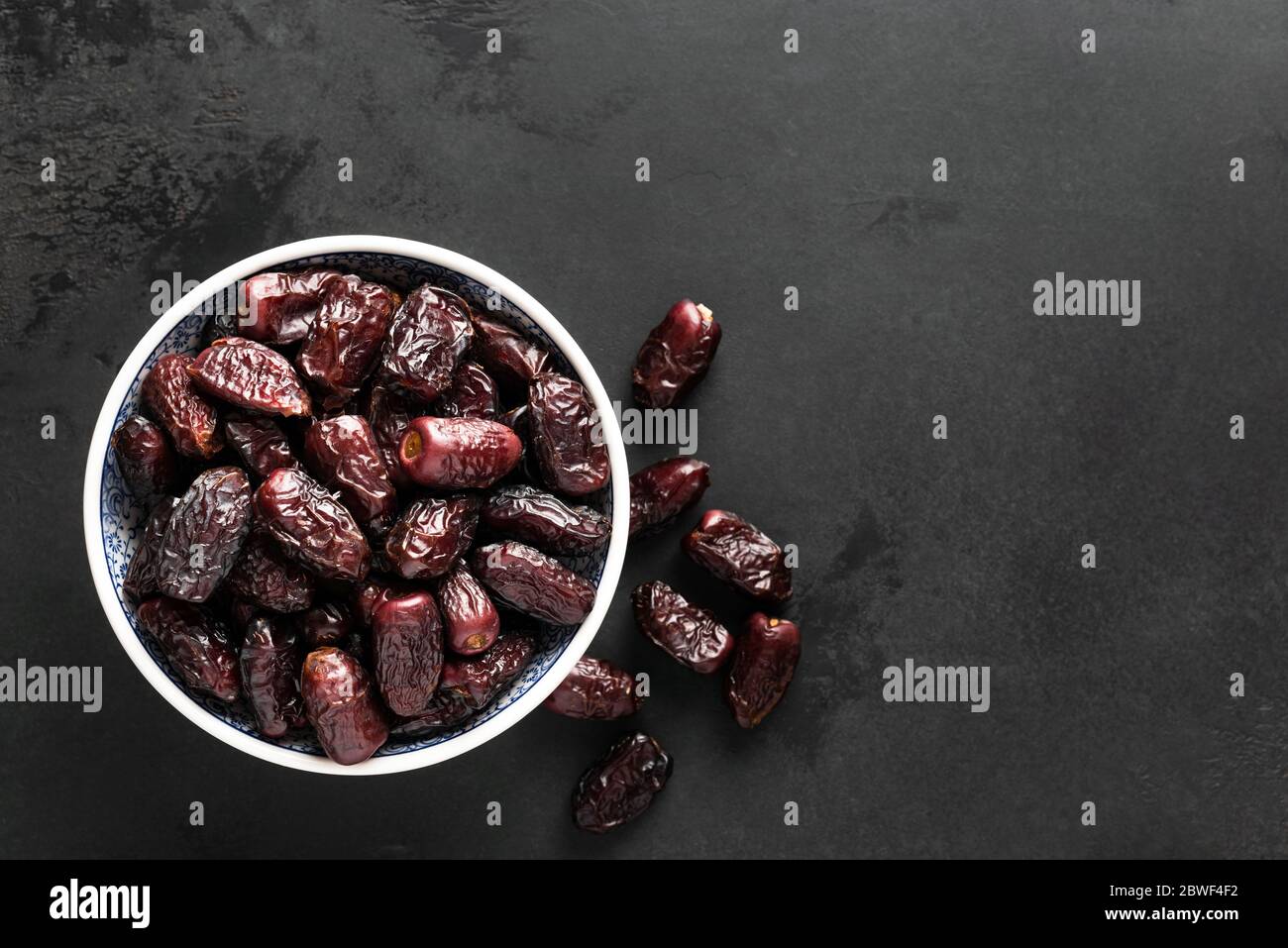 Dried dates in bowl on black background with copy space for text, top view. Black concrete background texture Stock Photo