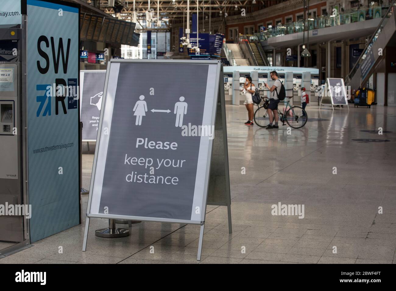 Face Covering and hand washing hygiene requesting signs stand within the Waterloo main station concourse, London, England, UK Stock Photo