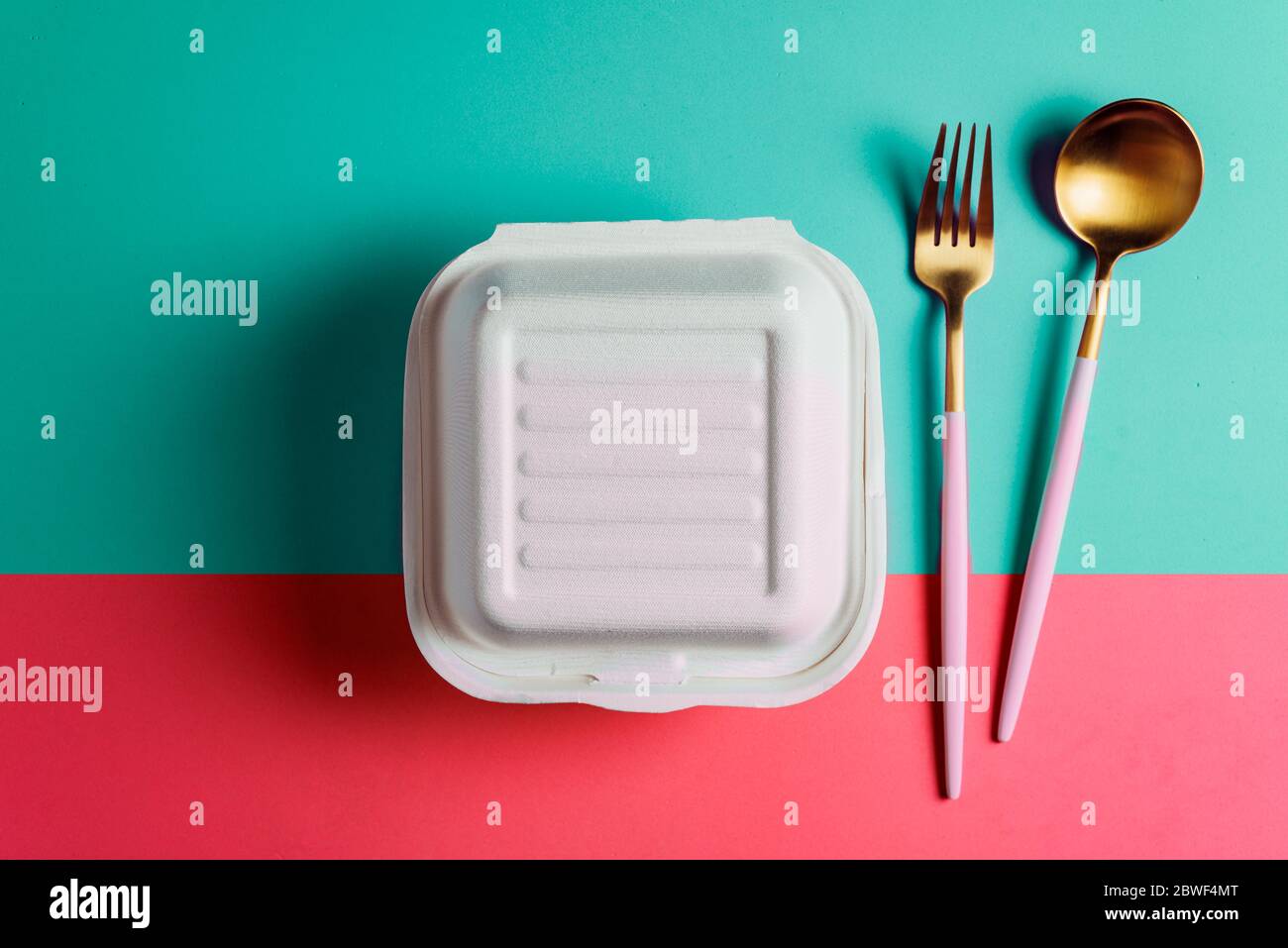 Healthy food concept: white burguer packaging closed with golden fork and spoon, in cardboard lunch box to take to the office on pink surface Stock Photo