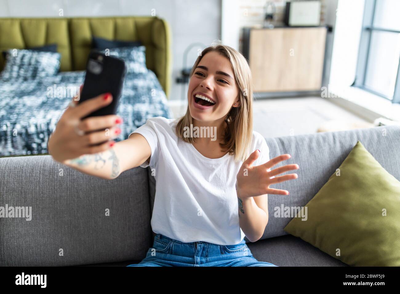 Photo of charming lady holding telephone making selfies speaking skype waving palm saying hi sitting comfort sofa wear casual checkered shirt apartmen Stock Photo