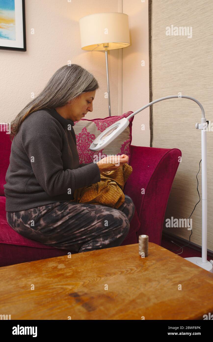 Woman sewing using illuminated magnifying glass to help with fine detail work. Stock Photo