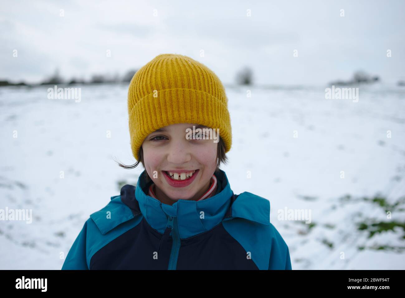 Happy smiling child in yellow hat outside in cold snowy winter weather Stock Photo