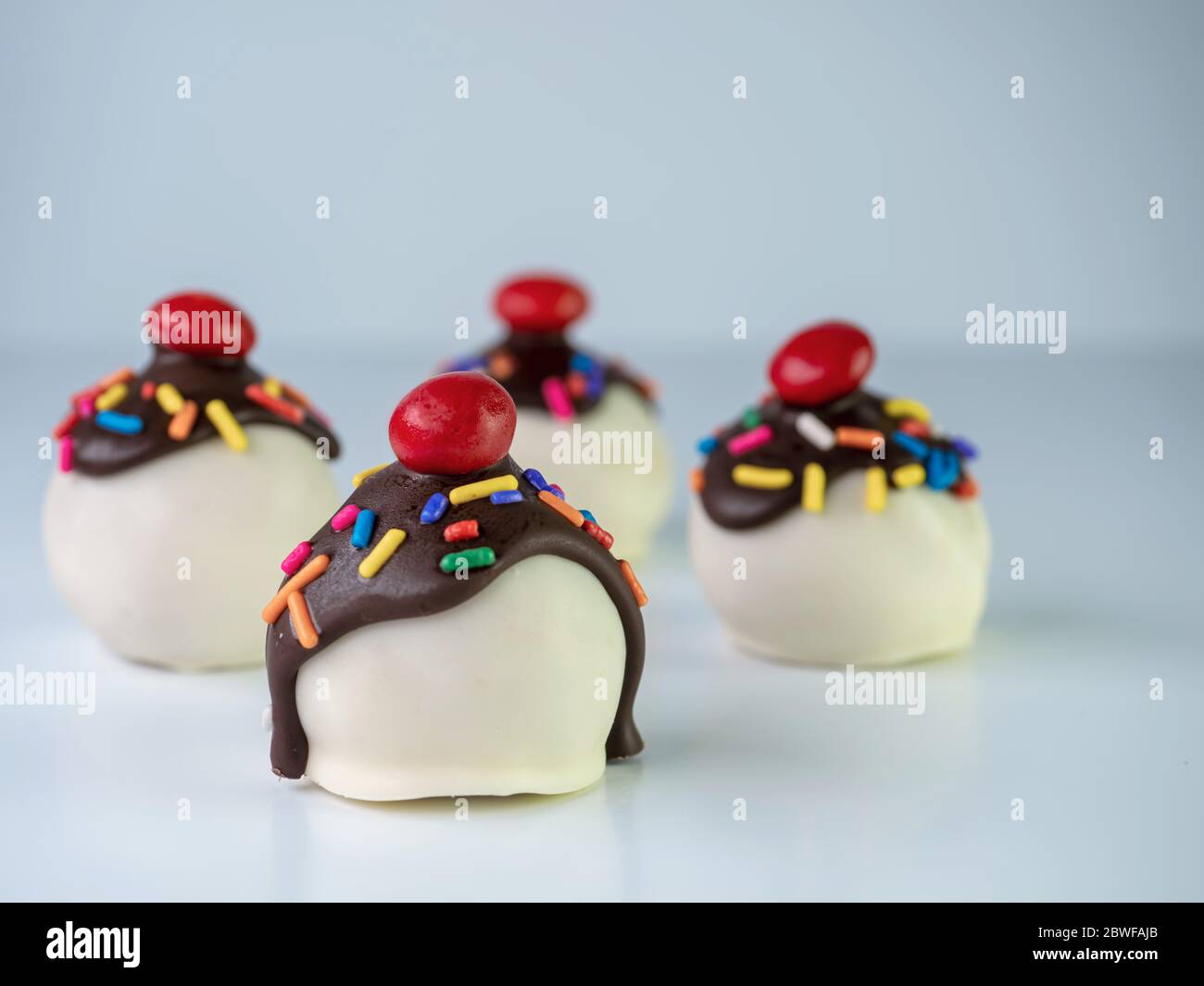 Banana split cake balls with white coating and chocolate drizzled on along with sprinkles and a cherry on top!  Mini truffle dessert, delicious and co Stock Photo