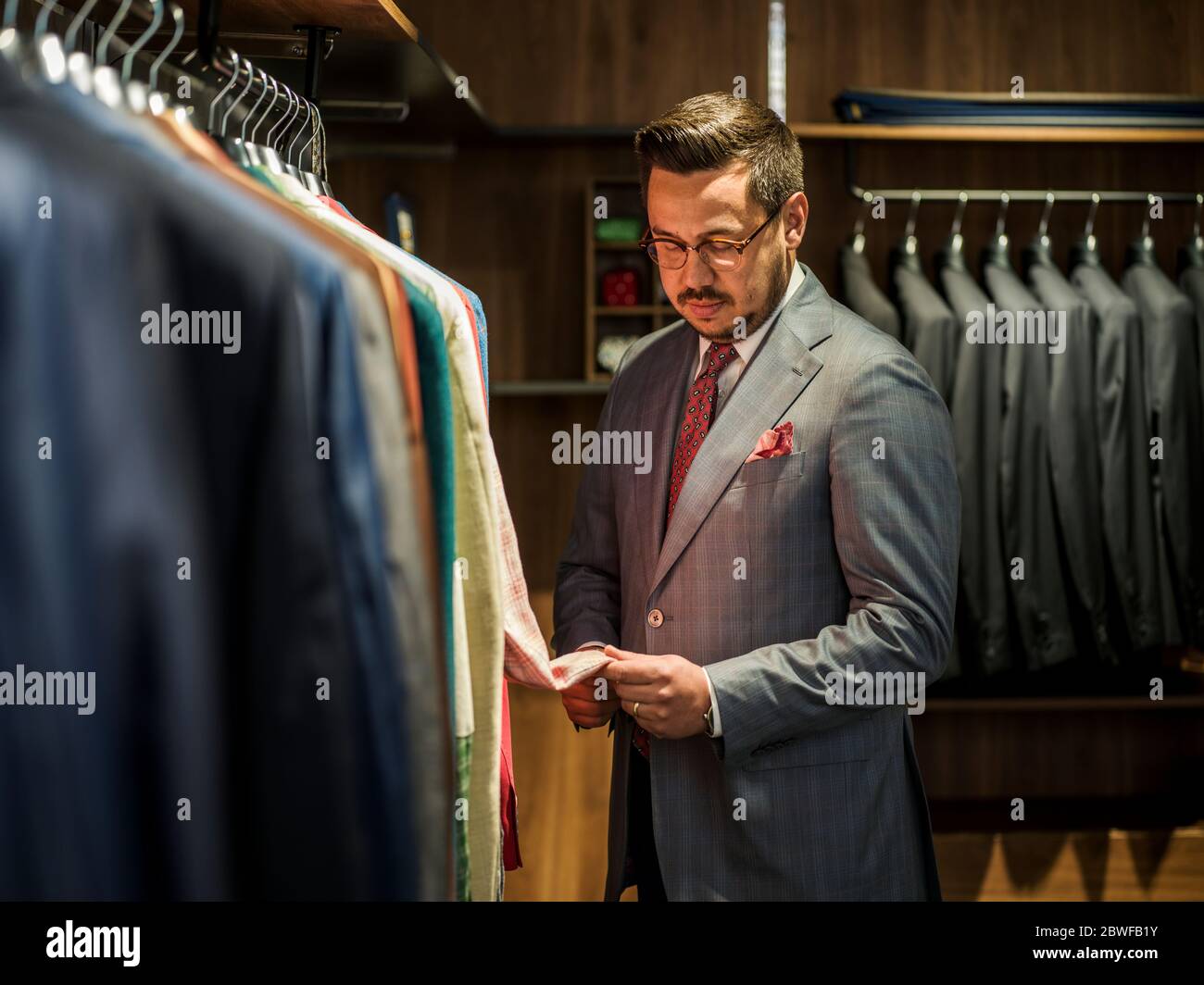 Young handsome man in costume looking for jacket in shop Stock Photo