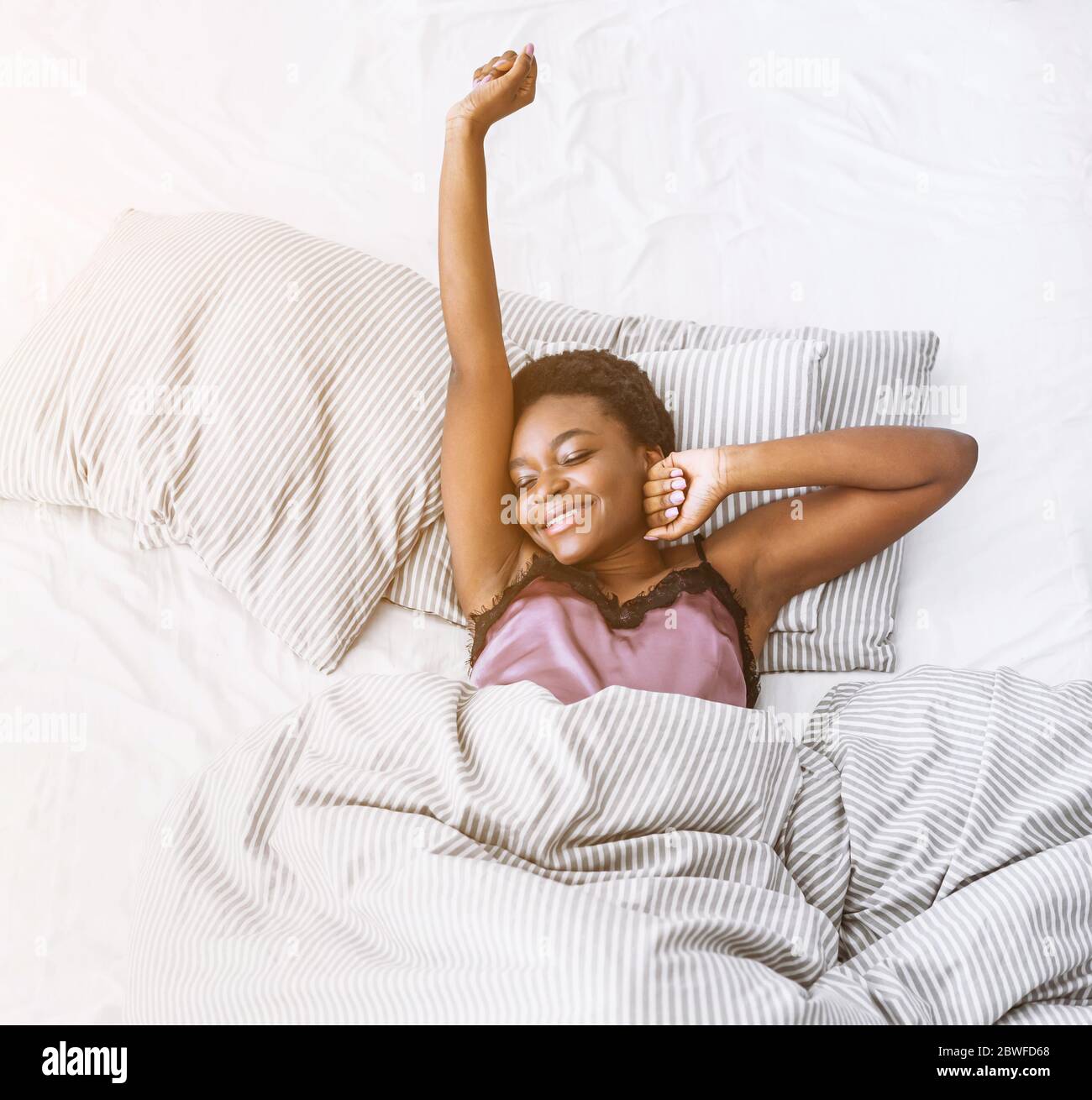 Start of sunny day. Smiling african american girl stretching in bed Stock Photo